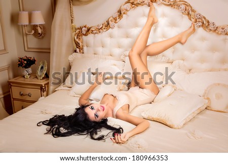 Beautiful and attractive young adult female brunette sensuality woman posing on bed in exclusive apartment