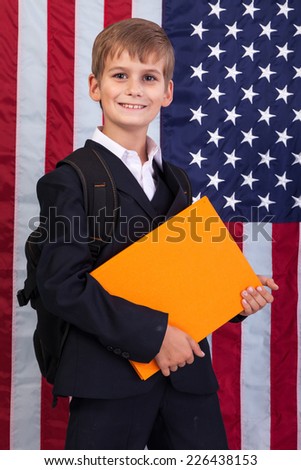 Ã?Â??ute schoolboy is holding an orange book against USA flag