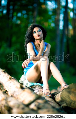 Beautiful Young Woman sitting on log posing on a warm summer day