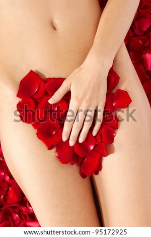 Beautiful body of woman against petals of red roses. Heart shape made out of rose petals