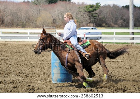 Young blonde woman barrel racing; a young woman turns around a barrel and races to the finish line