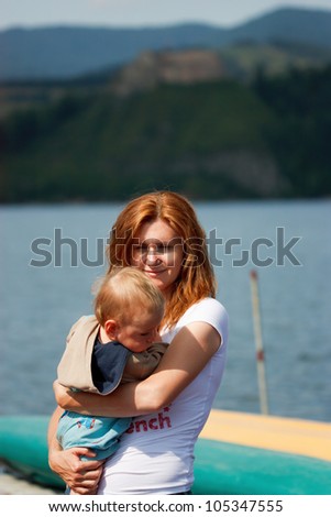 Mother holds in arms her baby on lake background