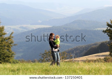 Mother is walking with child on meadow in mountains summer
