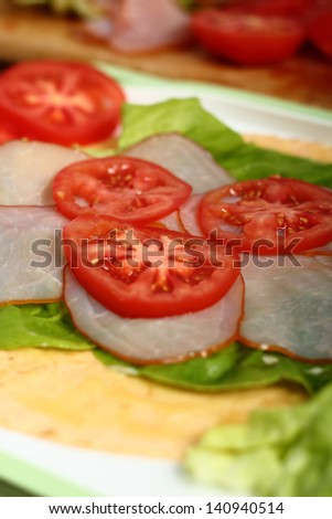Making wrap tortilla sandwich with ham, tomato, lettuce.