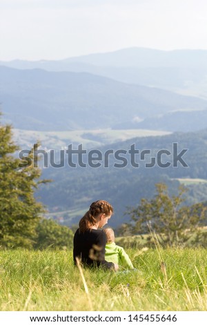 Mother sitting with child on meadow in mountains summer