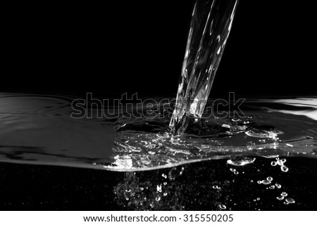Stream of water pouring into water at black background. Close up.