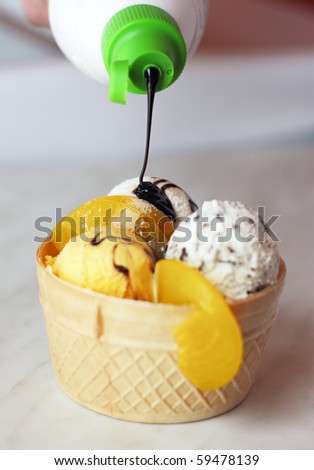 Ice cream in waffle bowl being poured chocolate syrup