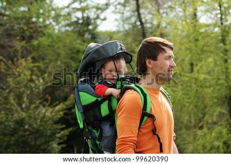 Young father is hiking with 1 year old son in baby carrier