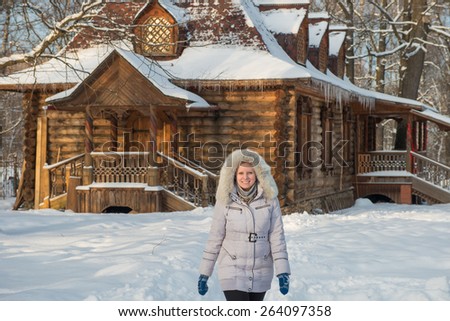 Girl walking in winter park on a background of a wooden house