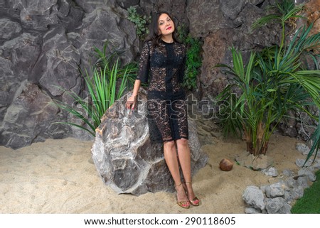 Beautiful woman in a black dress is sitting on a large rock