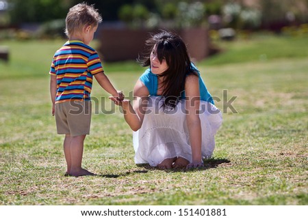 A young toddler giving something to he's beautiful mother while they are on the grass in summer.