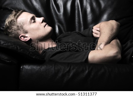 Young man sleeping on a black leather couch.