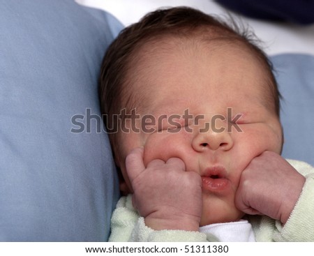 Close up of a beautiful baby boy sleeping with he\'s fists on he\'s cheeks.