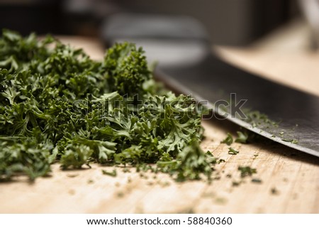 Closeup of freshly cut parsley next to a knife on a wooden cutting board.