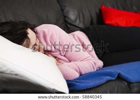 Studio shoot of a beautiful young woman resting on the black leather couch on top of a blue woven blanket. Her head is resting on a white pillow.