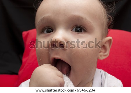 Studio close up of a cute baby boy with a dirty mouth, with red pillows behind him and a black background.