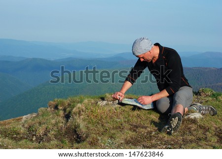 Summer in the Carpathian Mountains. Hiker sitting on top, looking at the map