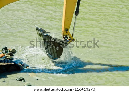 excavator machine during earthmoving in a river, logos removed