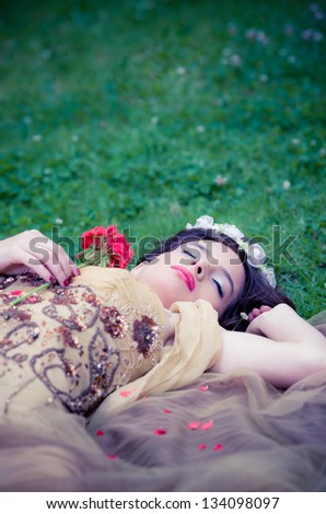 SLEEPING BEAUTY lying on the grass in the forrest with a rose