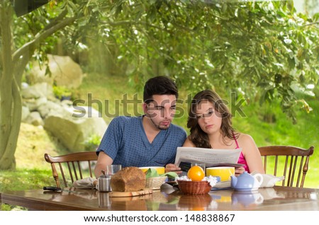 Couple having healthy breakfast at home, eating cereals drinking coffee, and reading newspaper.