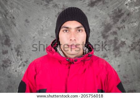 closeup of young handsome man wearing red jacket and black beanie over grey background