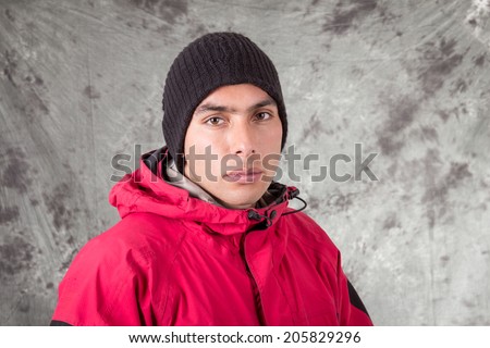 closeup of young handsome man wearing red jacket and black beanie over grey background