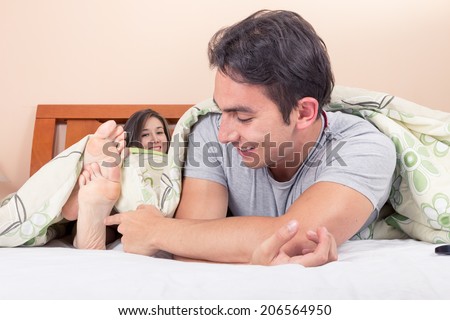 cute young man tickling girlfriends\' feet in bed
