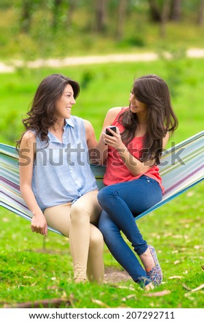 Two young girls sitting on a hammock looking at cell phone and laughing