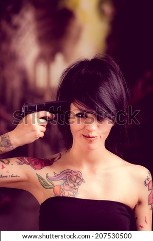 Beautiful tattooed girl with attitude holding gun pointing to her head selective focus