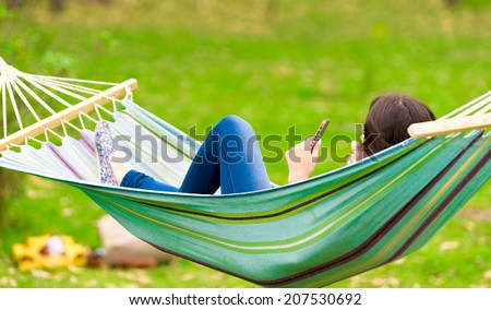 young girl lying on a hammock while using cell phone