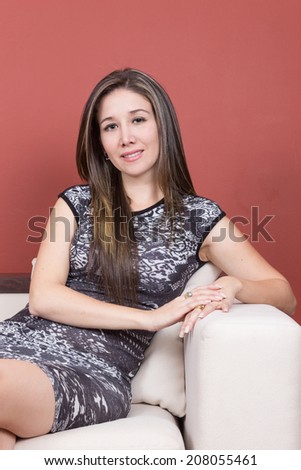 Beautiful young elegant girl wearing grey dress sitting on white sofa in livingroom
