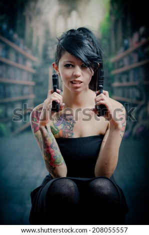 provocative tattooed girl in black dress poiting guns up