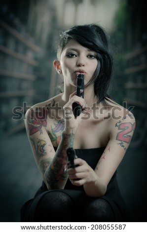 provocative tattooed girl in black dress blowing one gun and pointing front the other one