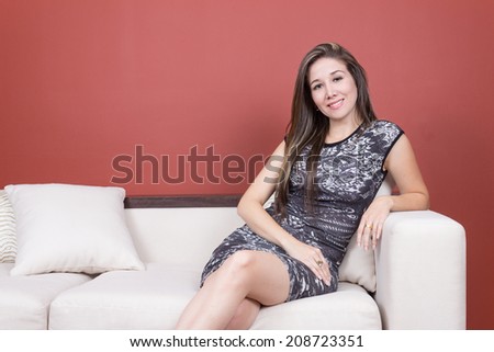 Beautiful young elegant girl wearing grey dress sitting crossing her legs in white sofa