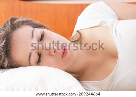 Attractive young woman sleeping in bed resting head on white pillow