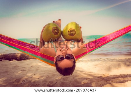 Beautiful young girl lying in a hammock on relaxing beach holding two coconuts