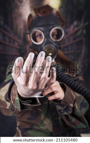 Young girl wearing military uniform and gas mask with plastic gloves over dark background selective focus