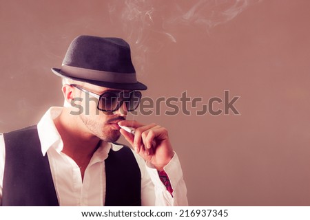 Young handsome stylish male model wearing a hat smoking a cigarette