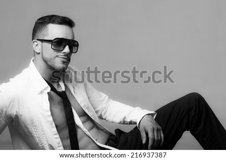 Sexy young male model wearing sunglasses sitting with unbuttoned shirt black and white portrait