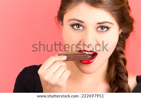 pretty young brunette girl eating chocolate over red background closeup