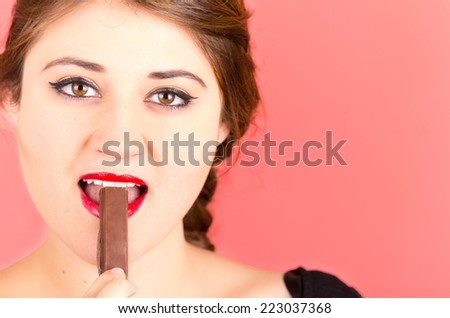 pretty young brunette girl eating chocolate over red background closeup