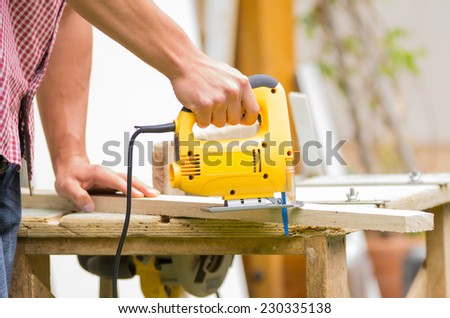 young man carpenter builder working with electric jigsaw and wood