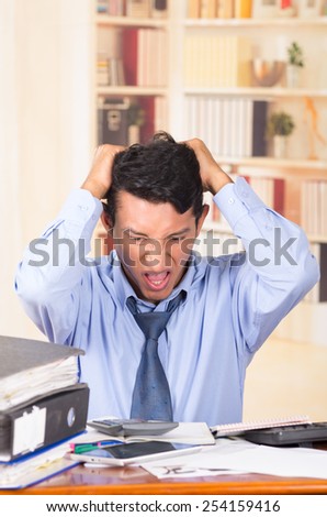 young stressed angry overwhelmed business man with piles of folders on his desk