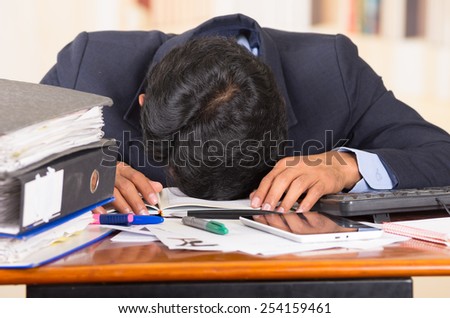 young stressed overwhelmed business man with piles of folders sleeping on his desk
