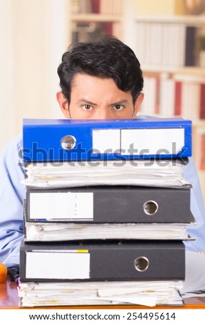 young stressed overwhelmed business man with piles of folders on his desk