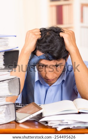 young stressed overwhelmed business man with piles of folders on his desk with tie on his head