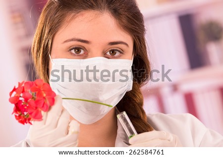 young female biologist wearing mask testing with red flower in lab