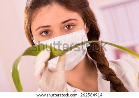 closeup portrait of young female biologist wearing mask experimenting with leaf in lab