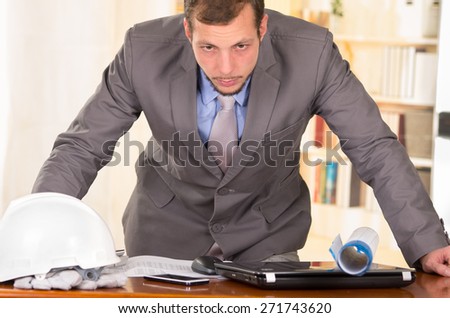 young handsome busy architect leaning on his desk working looking stressed