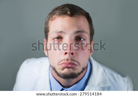 Closeup portrait of sad young doctor crying over gray background